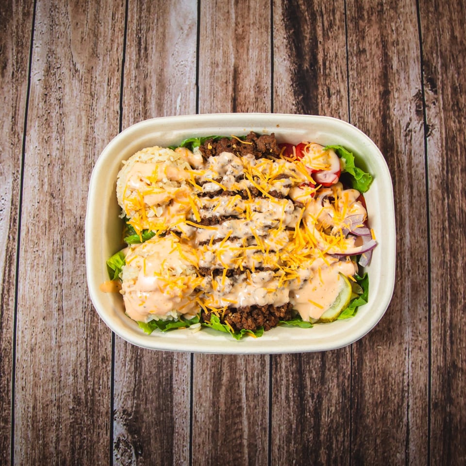 Overhead view of a burger bowl with ground beef, rice, lettuce, cheese, and sauce on wood.