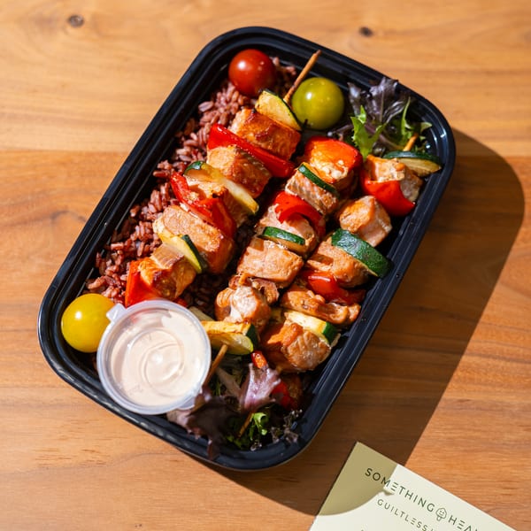 Something Healthy Guiltless Kitchen meal with chicken and vegetable skewers, rice, and a side of sauce.